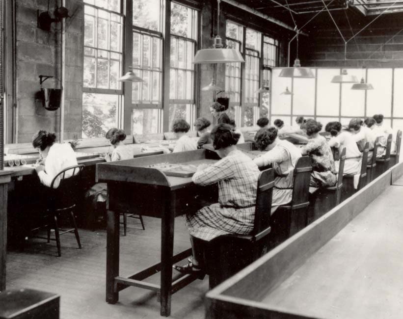 约 1922 年美国镭公司的工厂里，十几名年轻女工坐在长桌前低头描画表盘